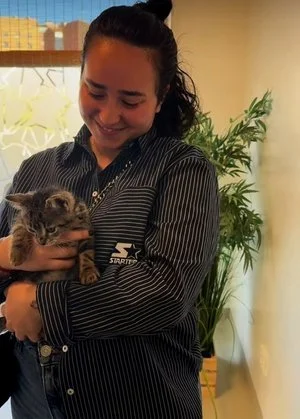 Mujer sonriendo mientras abraza a un gato. Fondo con plantas y ventanas