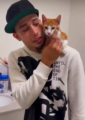 Joven sosteniendo un gato anaranjado y blanco cerca de su cara, con expresión cariñosa.
