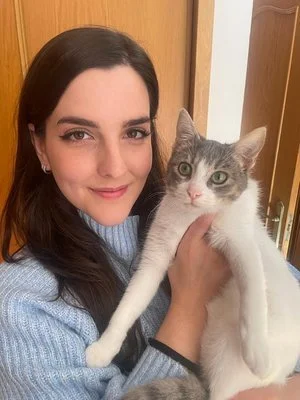 Una mujer sonriendo sostiene un gato gris y blanco en sus brazos.