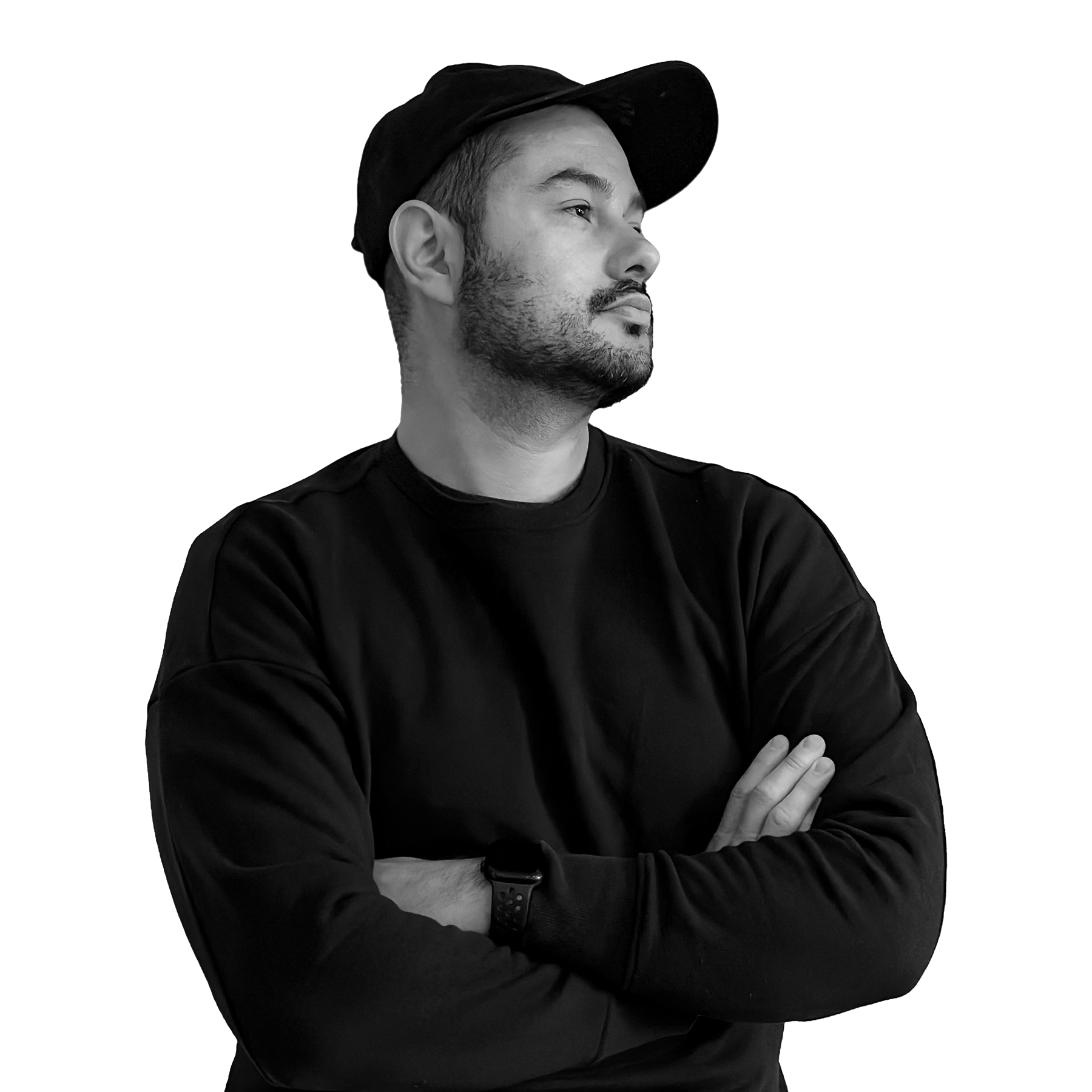 A man with a beard wearing a black cap and a black long-sleeve shirt, looking to the right with arms crossed.