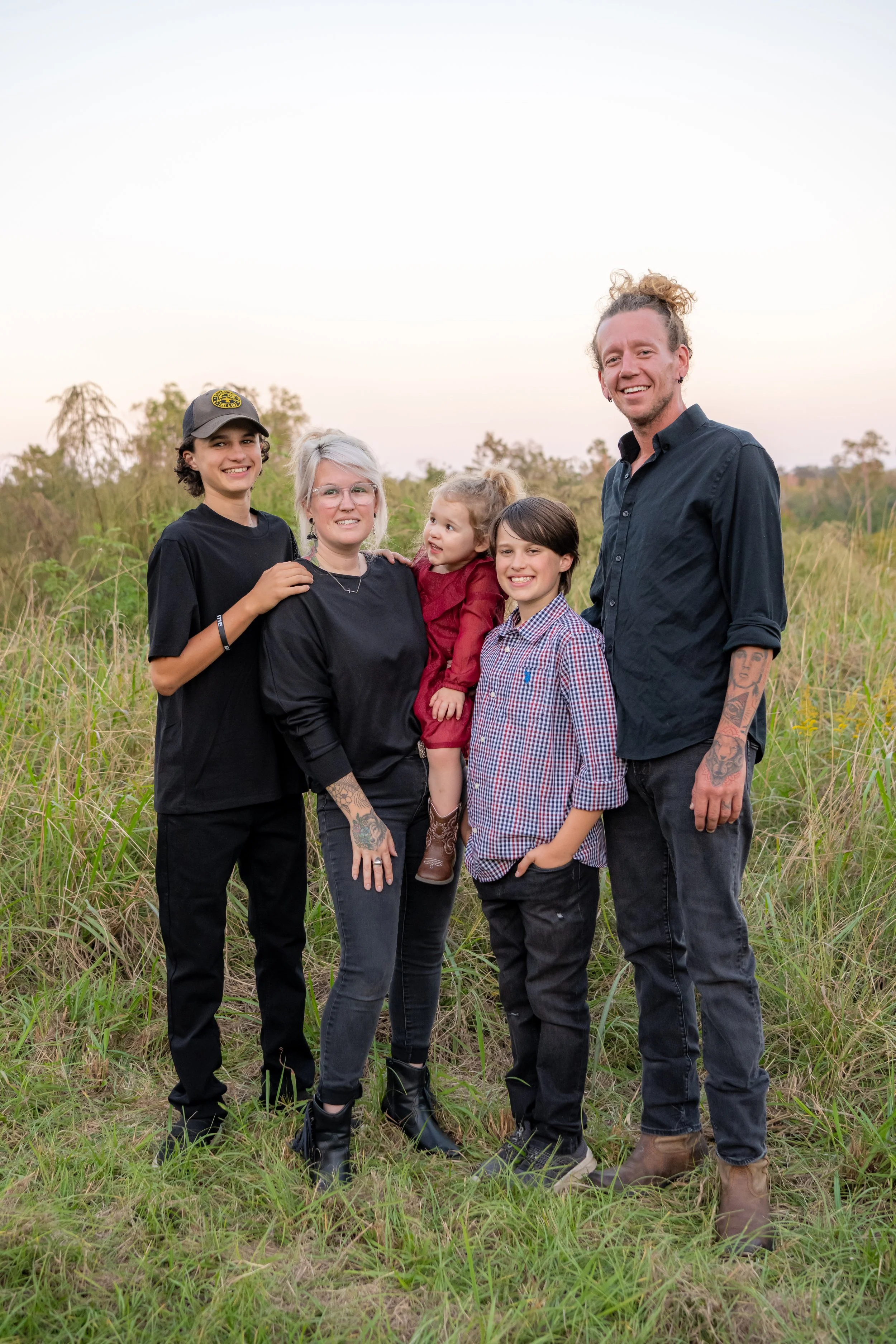 Group of five people, including children and adults, standing outdoors in a grassy field during sunset, smiling for the camera.