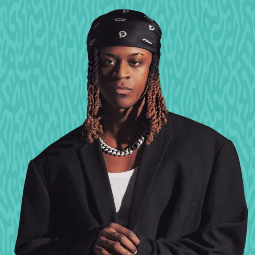 A young man with dreadlocks wearing a black bandana, black blazer, white T-shirt, and a silver chain necklace against a blue patterned background.