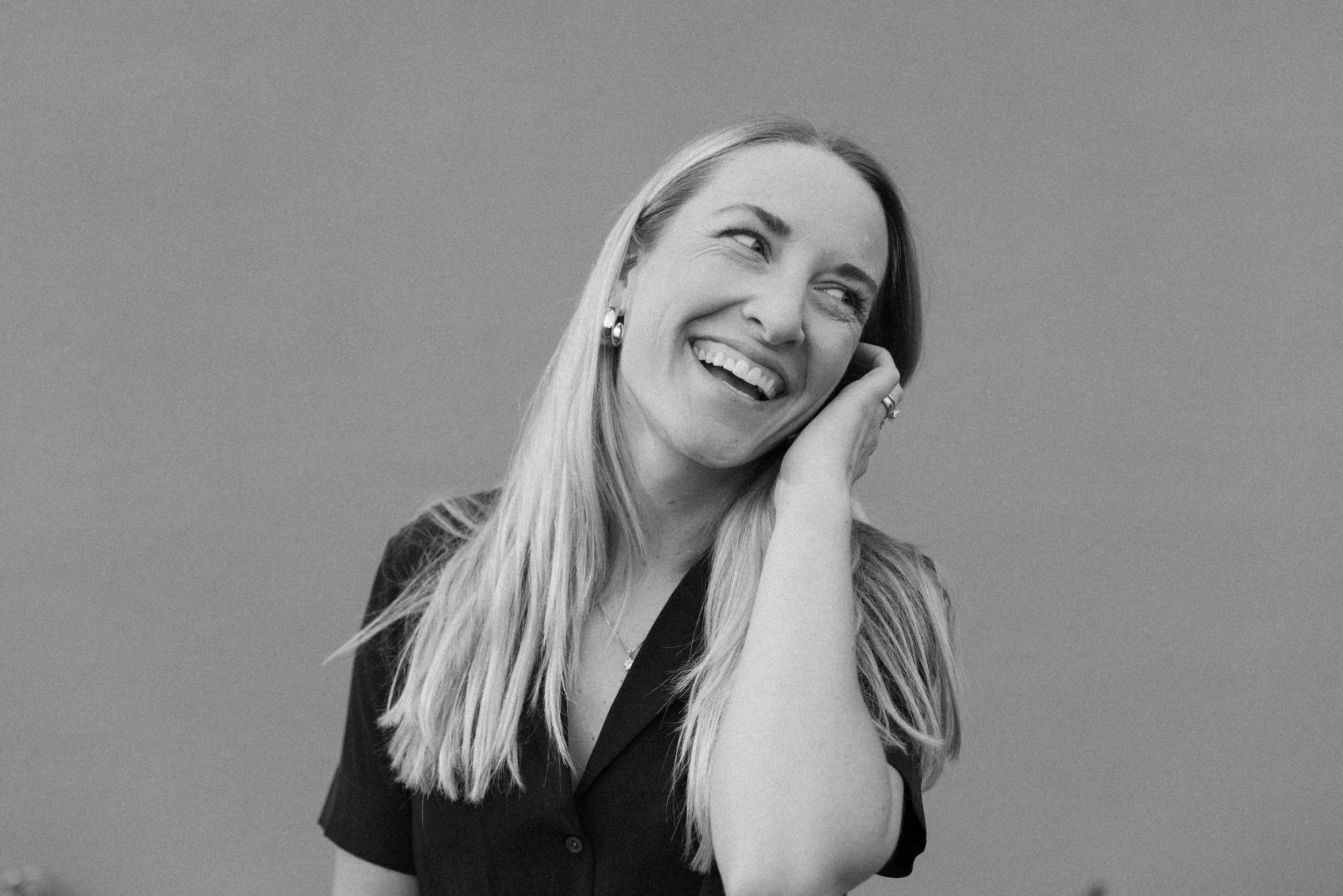 Ojai wedding photographer Katie Edwards stands and smiles in front of a clean, grey backdrop. Katie Edwards Photo is a top wedding photographer in California and specializes in Ojai weddings shot on film. Ojai Valley Inn wedding photographer