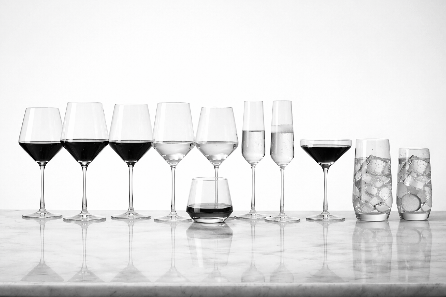 A row of different glasses with red wine, white wine, champagne, a glass of red wine, and two glasses with ice water, all on a marble surface with a white background.