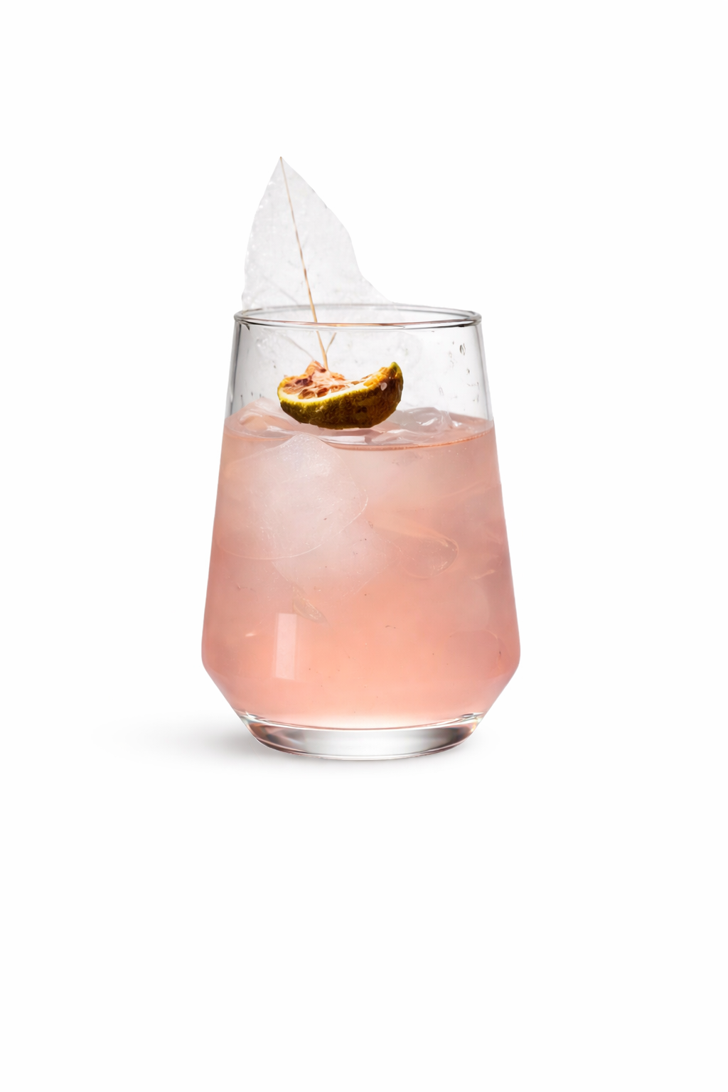 A pink cocktail in a glass, garnished with a slice of lime, ice cubes, a large ice shard, and a decorative leaf.