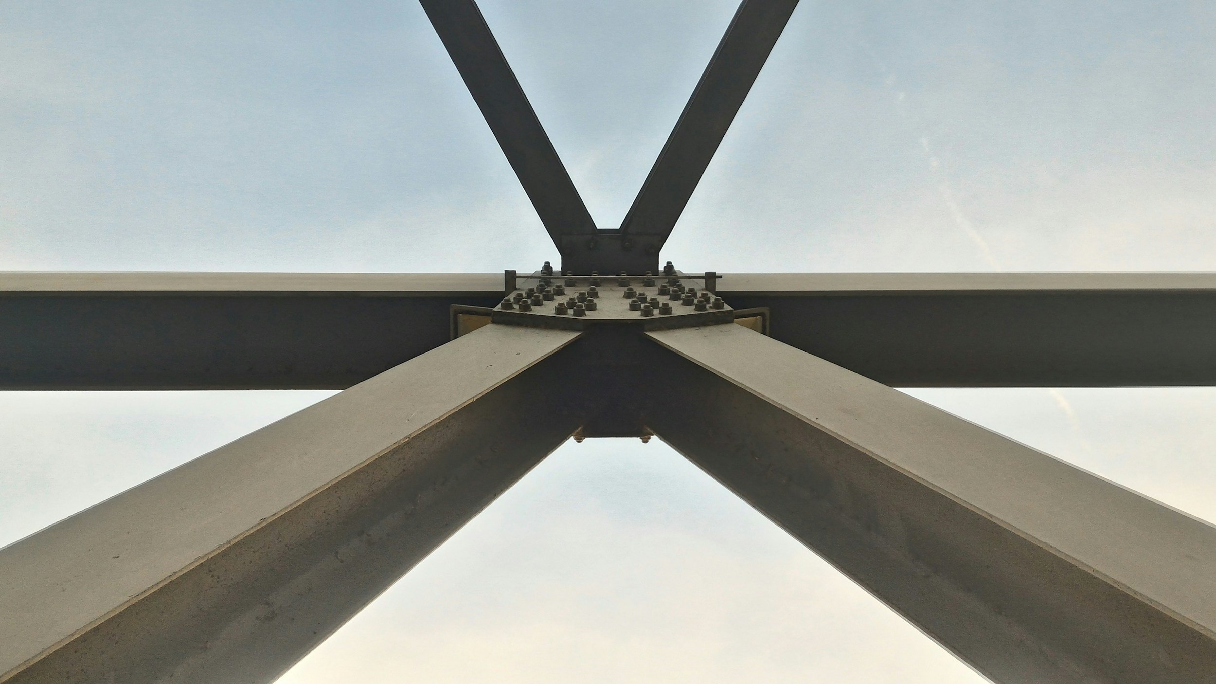Looking up at the structure of a steel transmission tower, showcasing the bolts and metal beams against the sky.