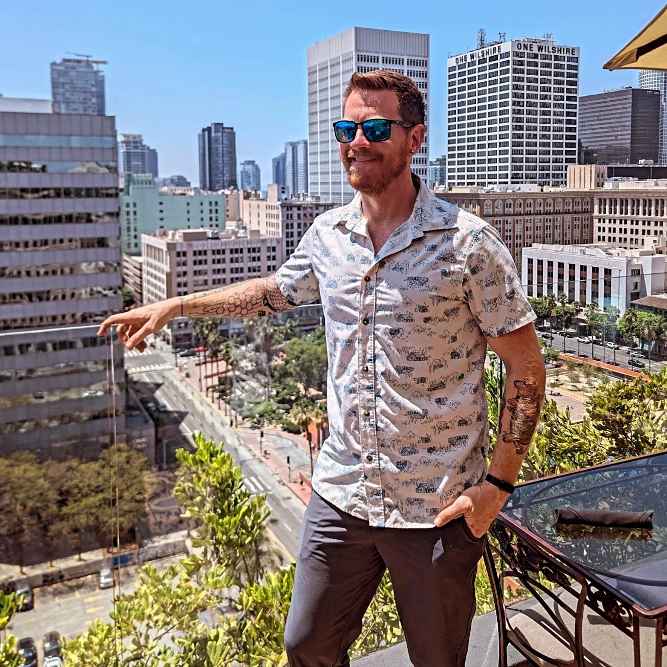 Man with sunglasses and tattoos on a balcony overlooking city skyline