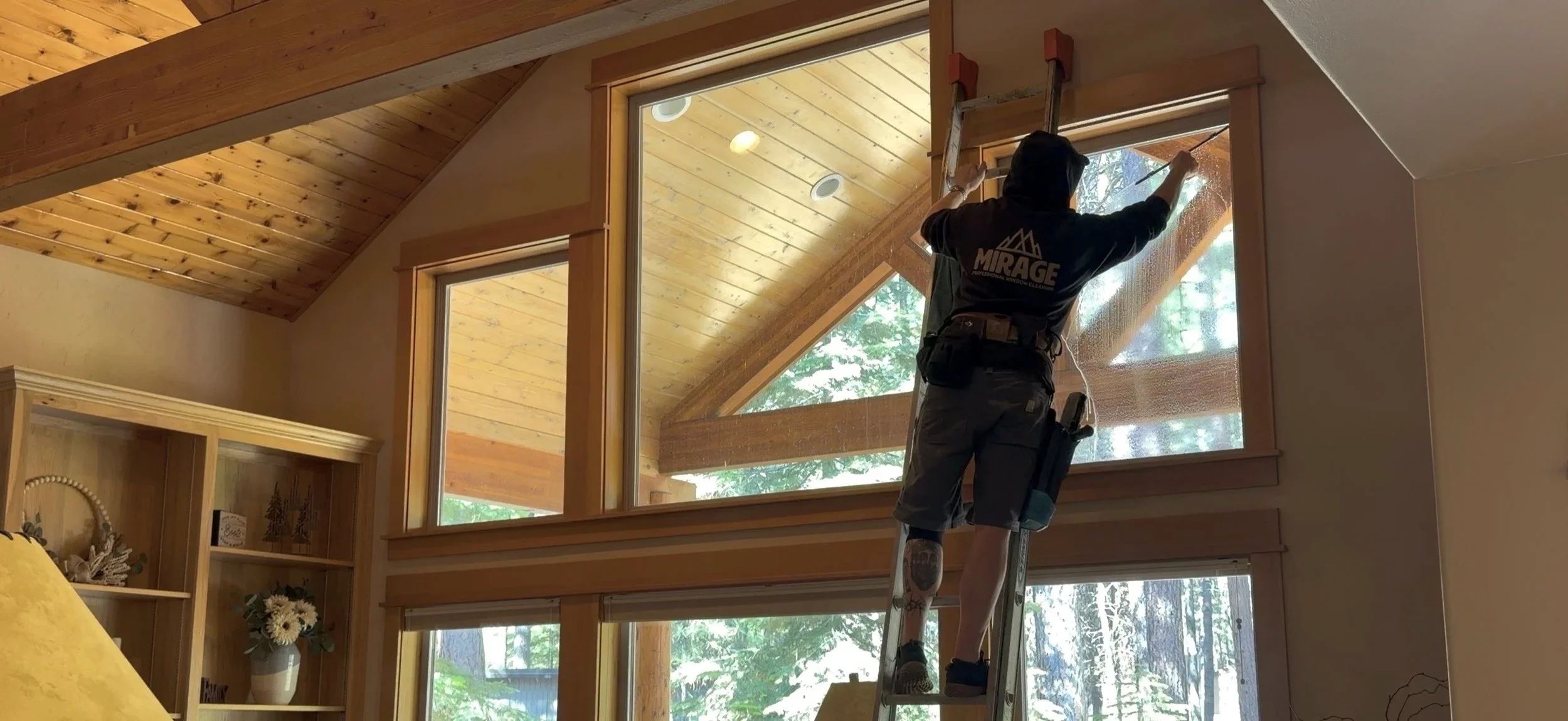 Person installing window screen on large triangular window in a wooden ceiling room.
