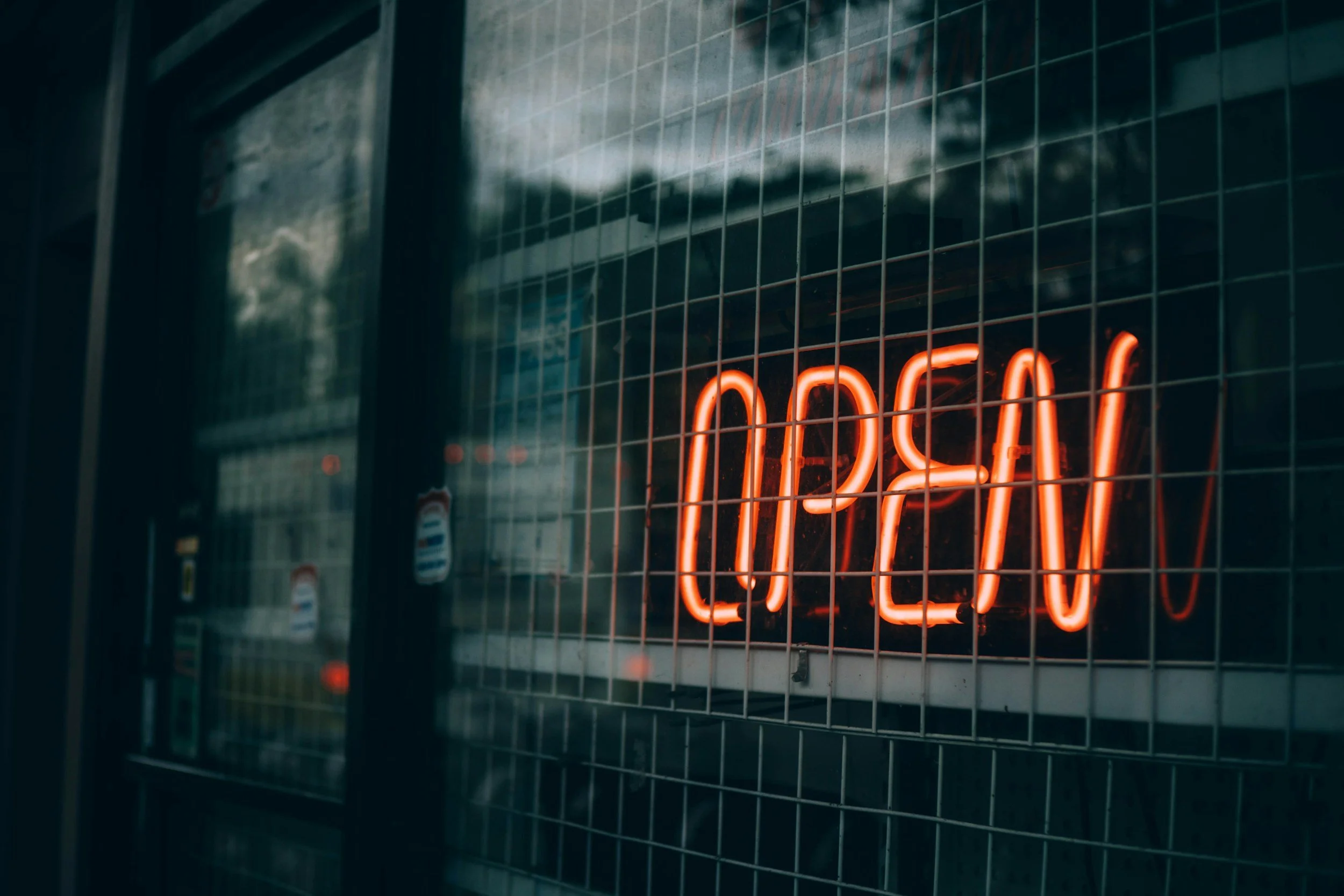 A neon sign displaying 'OPEN' in red letters, mounted on a metal grid outside a store or restaurant.