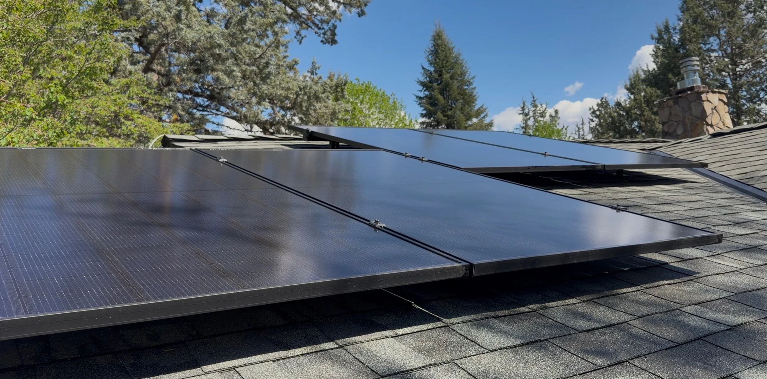 Solar panels installed on a house roof, with trees and a blue sky in the background.