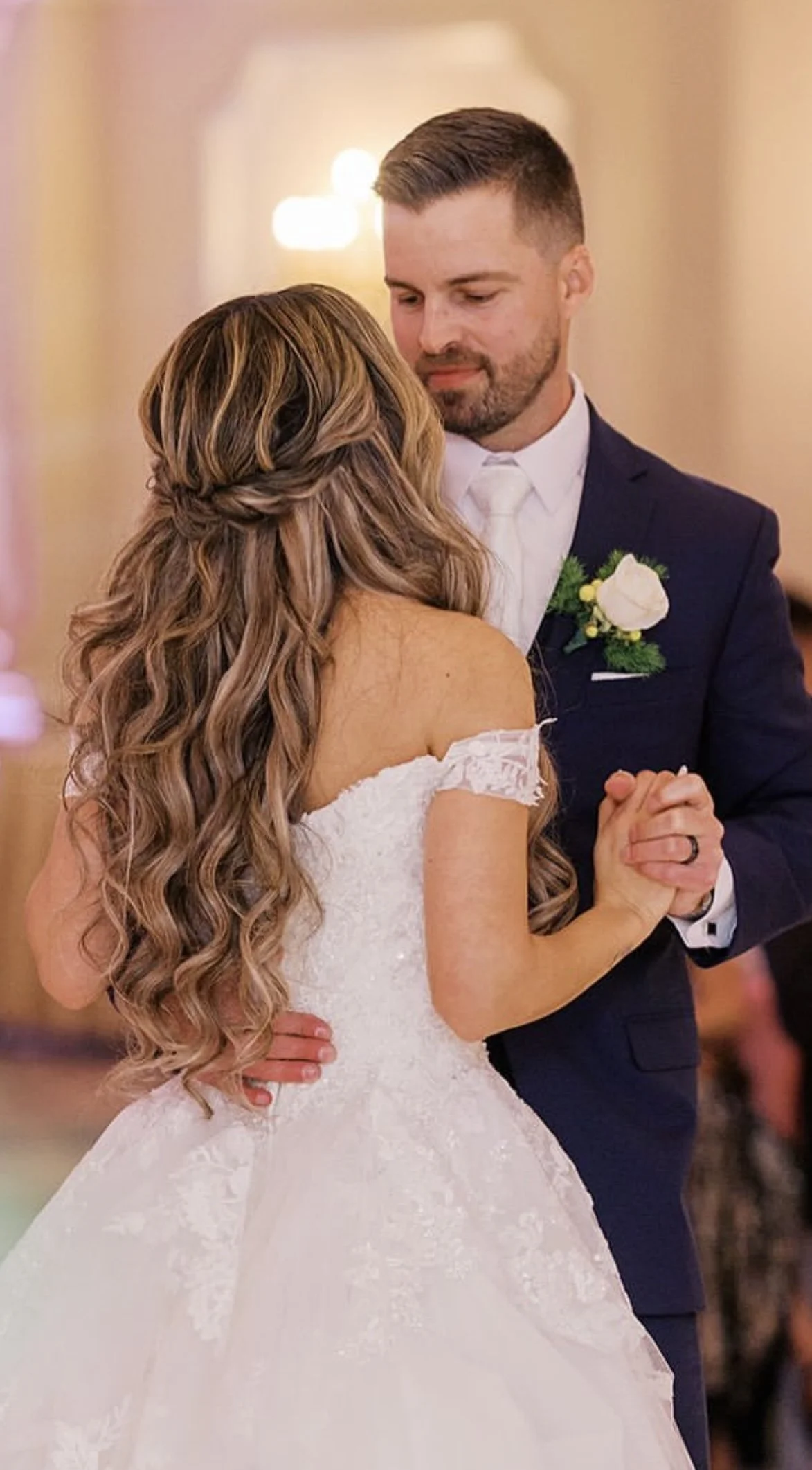 A bride and groom dancing at their wedding reception, holding hands and looking at each other lovingly.