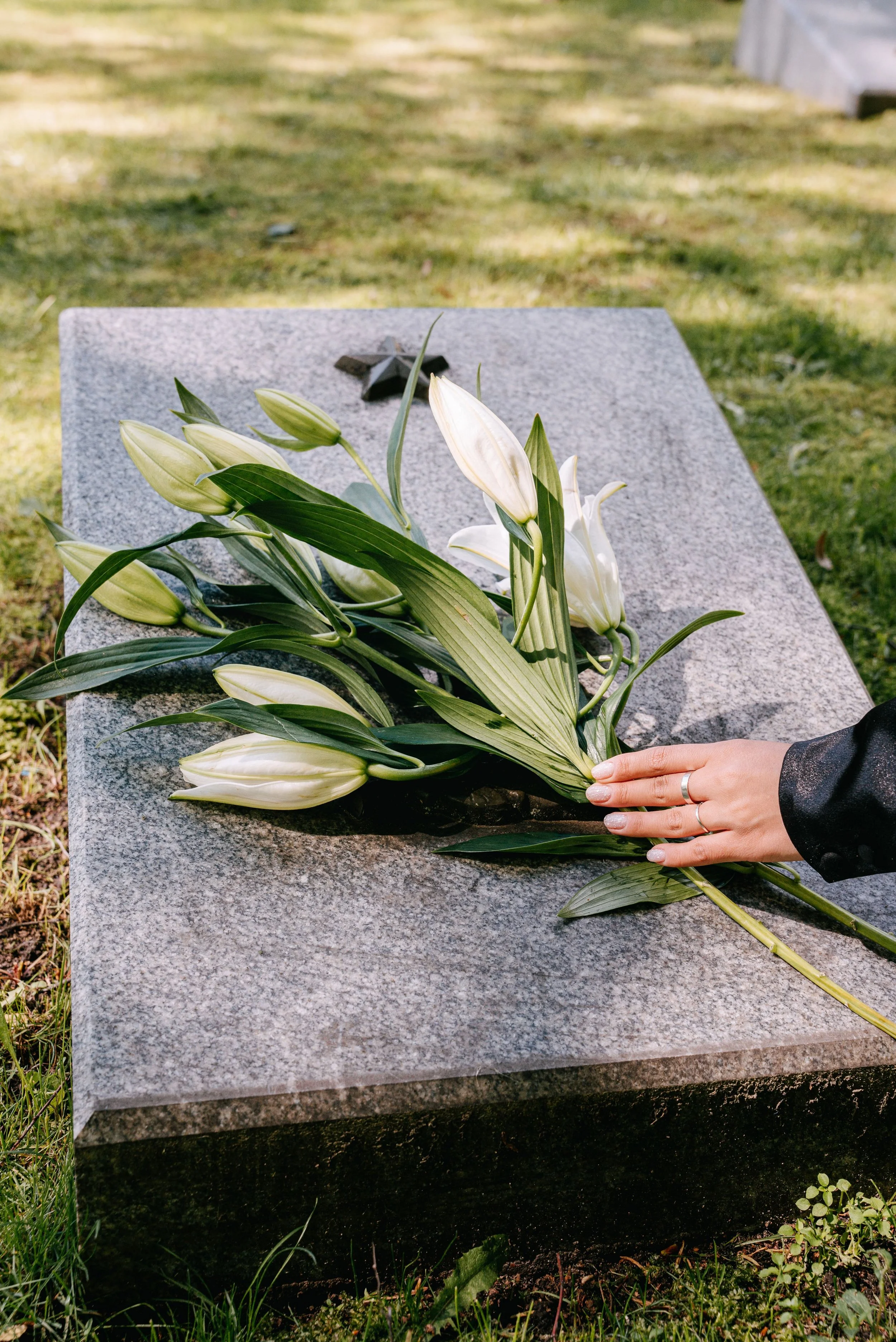 A hand placing white lily flowers on a granite grave marker — representing the compassionate estate cleanout support Home to Home Services provides for families after a senior passes in Richmond, VA and Washington, DC