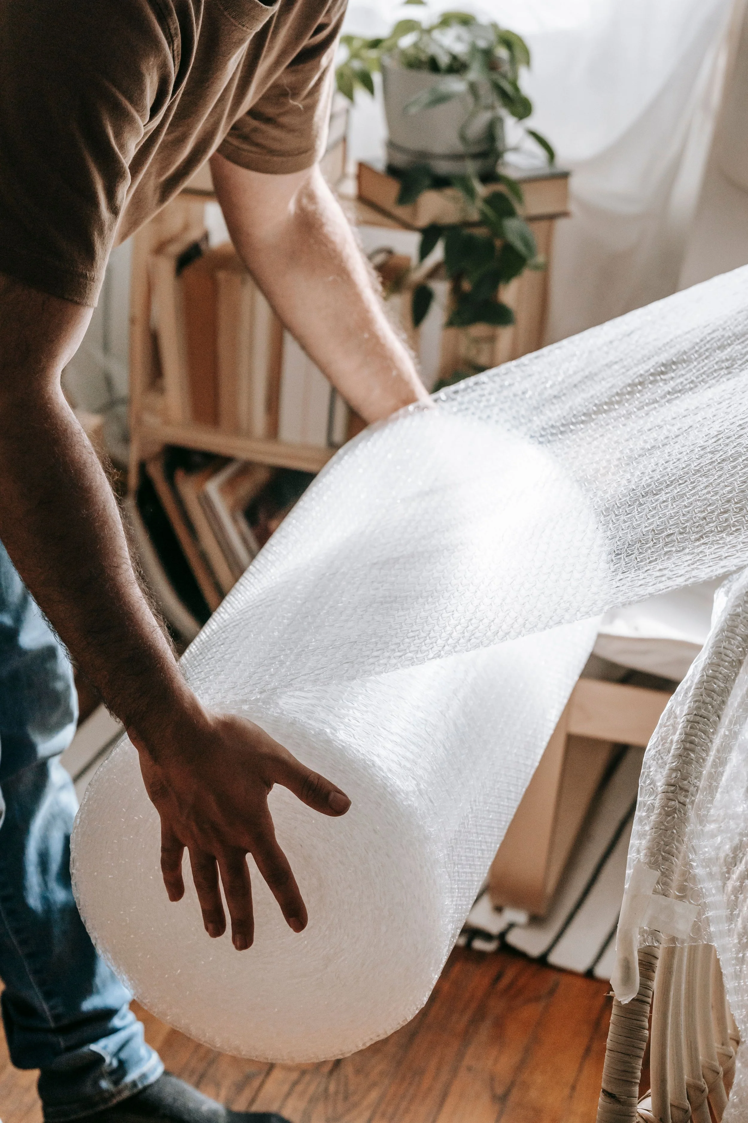 A professional packer unrolling a large sheet of bubble wrap to protect items for a move, with framed artwork visible in the background — demonstrating the careful, detail-oriented packing techniques used by Home to Home Services in Richmond, VA