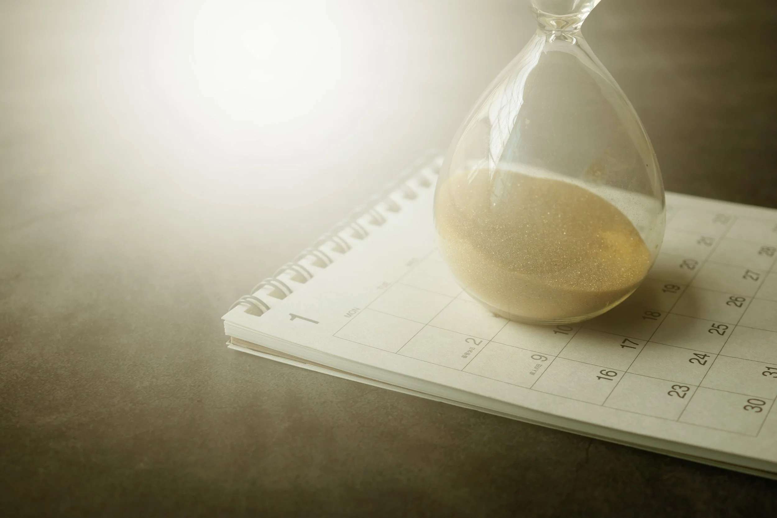 An hourglass with sand running out resting on an open calendar — representing the importance of booking a professional packing service far enough in advance before your move date, from Home to Home Services in Richmond, VA