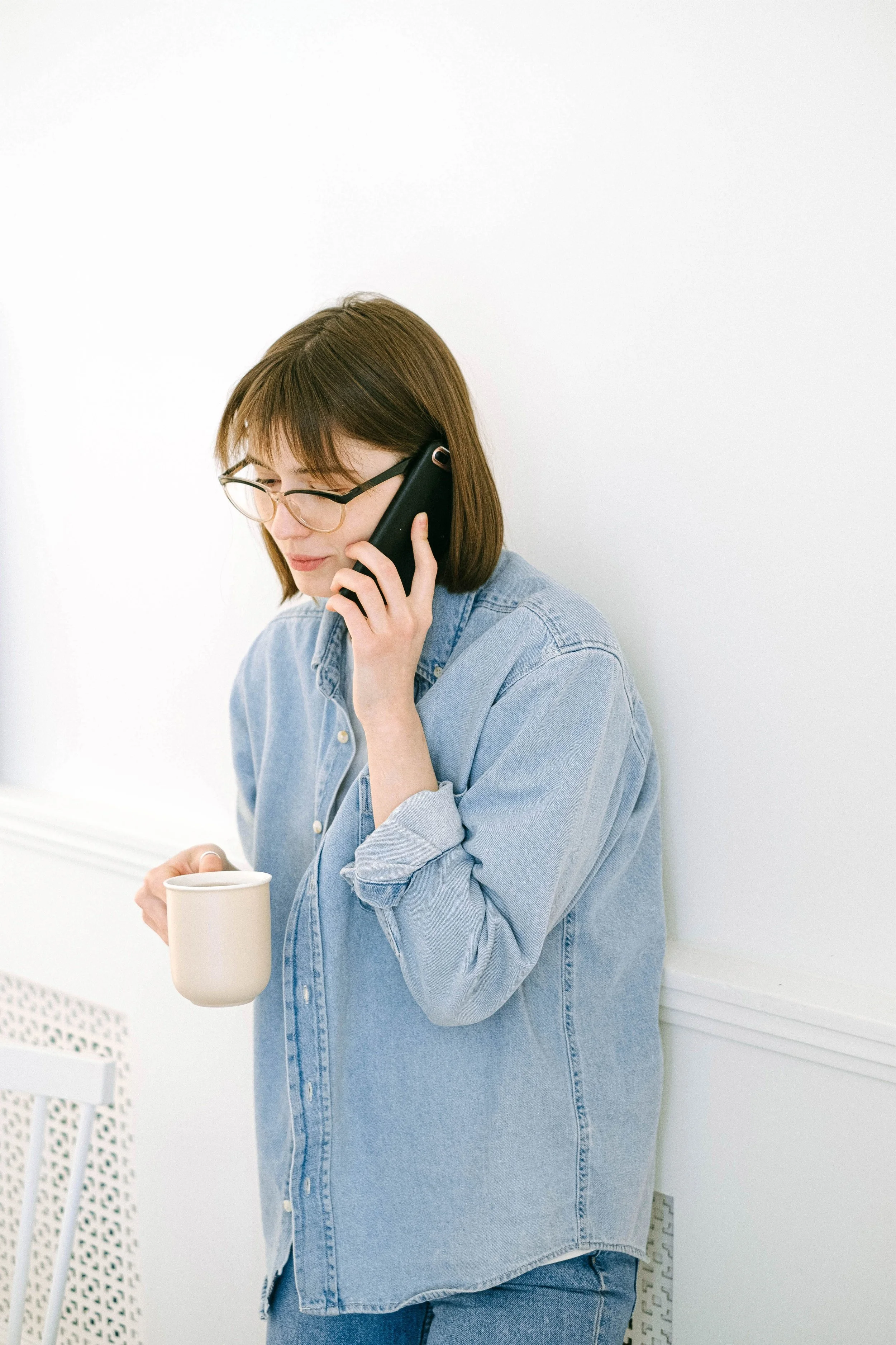 A woman holding a coffee mug and talking on the phone in a bright white room — representing the simple, low-pressure first step of calling to book a professional home organizing session with Home to Home Services in Richmond, VA