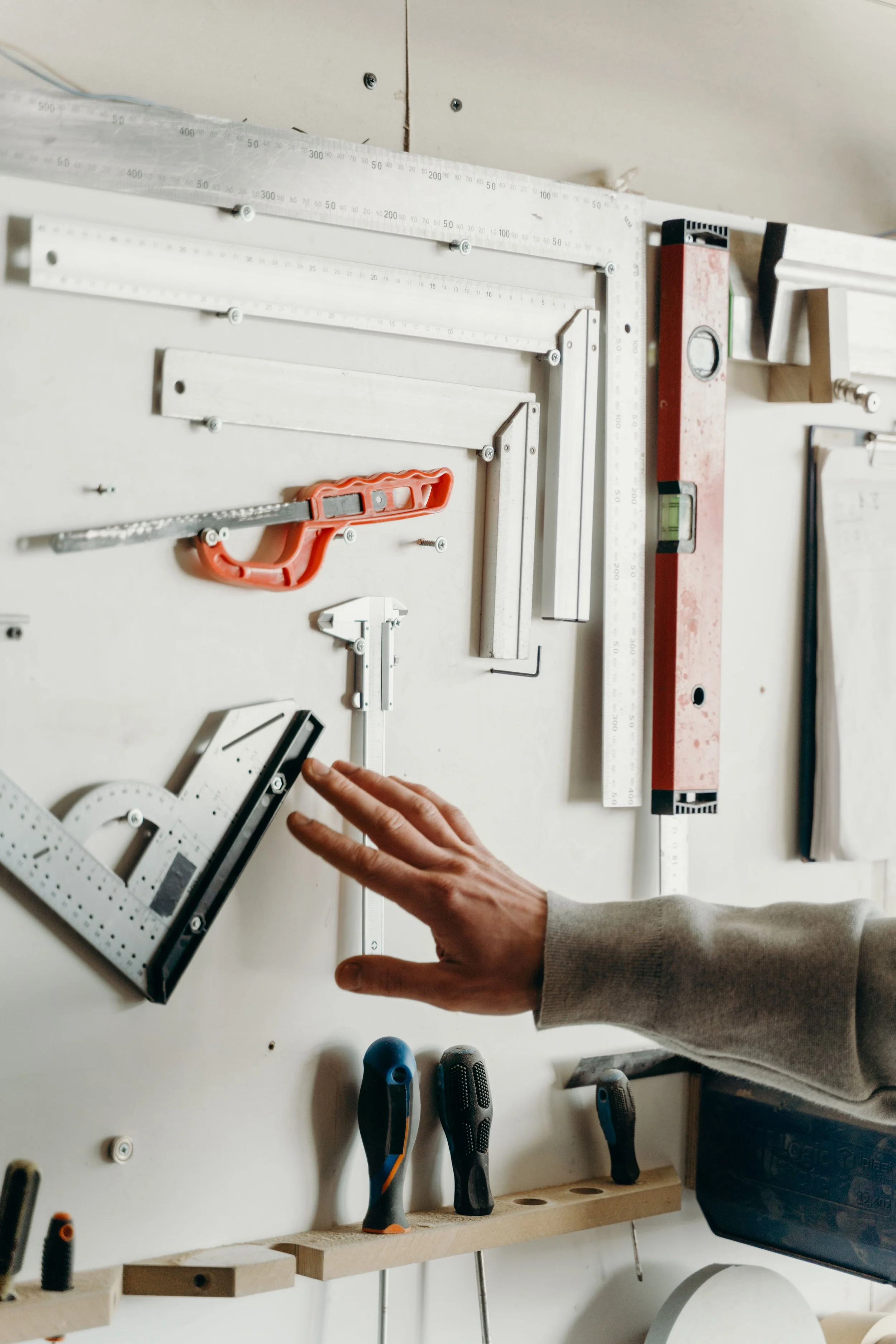 A hand reaching for a tool on a well-organized garage wall mount with rulers, a level, a utility knife, and screwdrivers arranged by category — representing the professional garage organization results Home to Home Services delivers in Richmond, VA