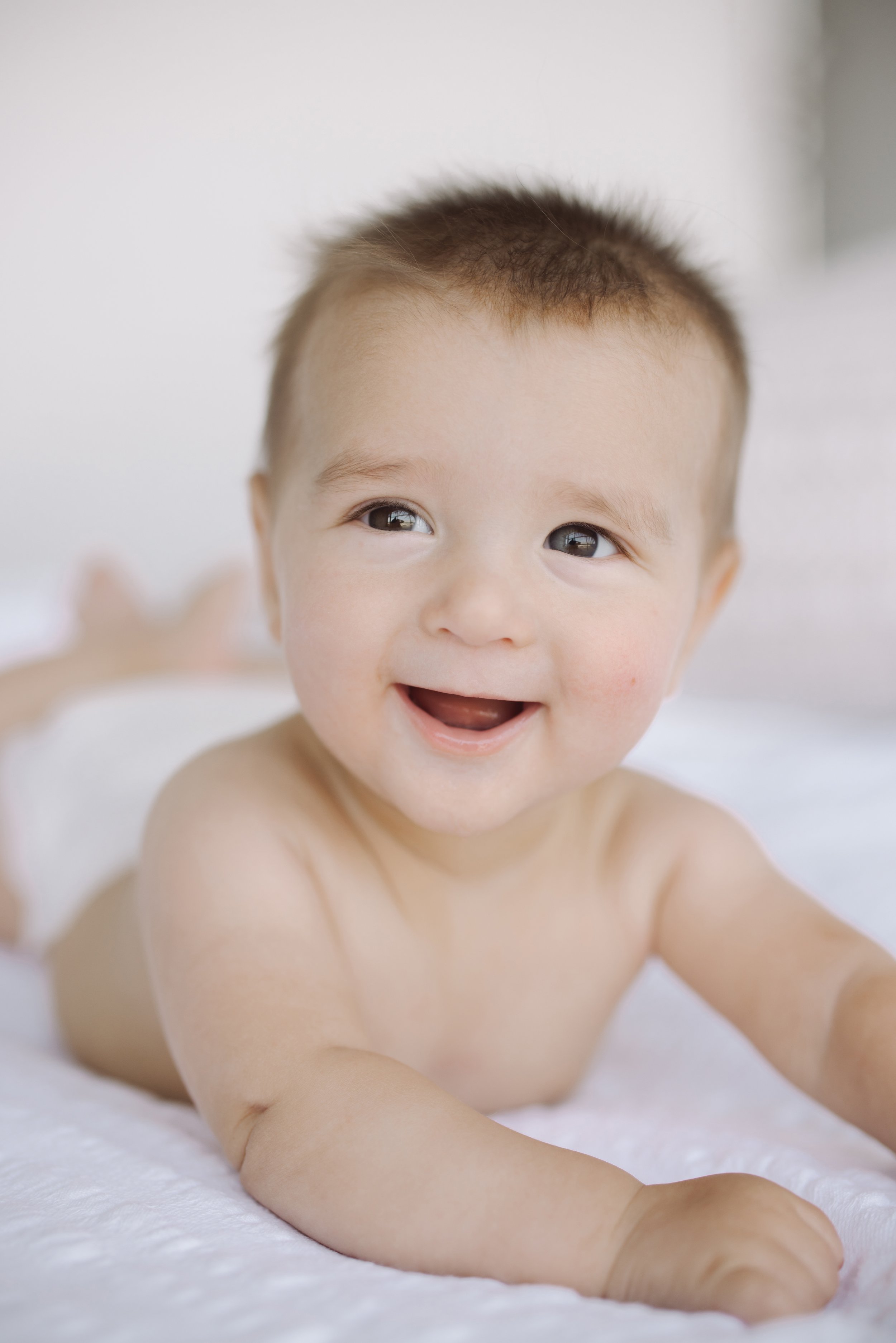 Smiling baby lying on a soft white surface.