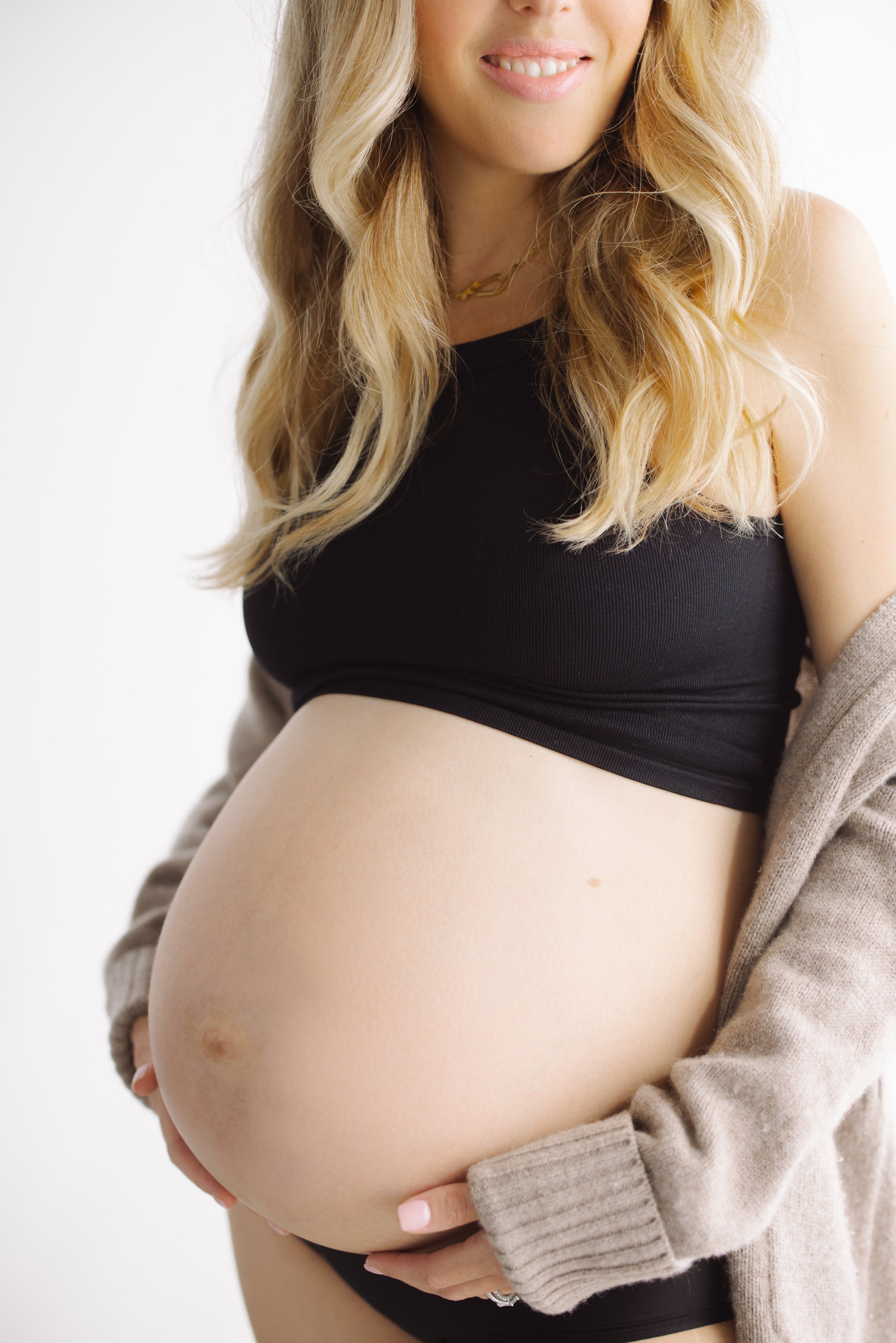 Pregnant woman holding her belly, wearing a black top and beige cardigan.