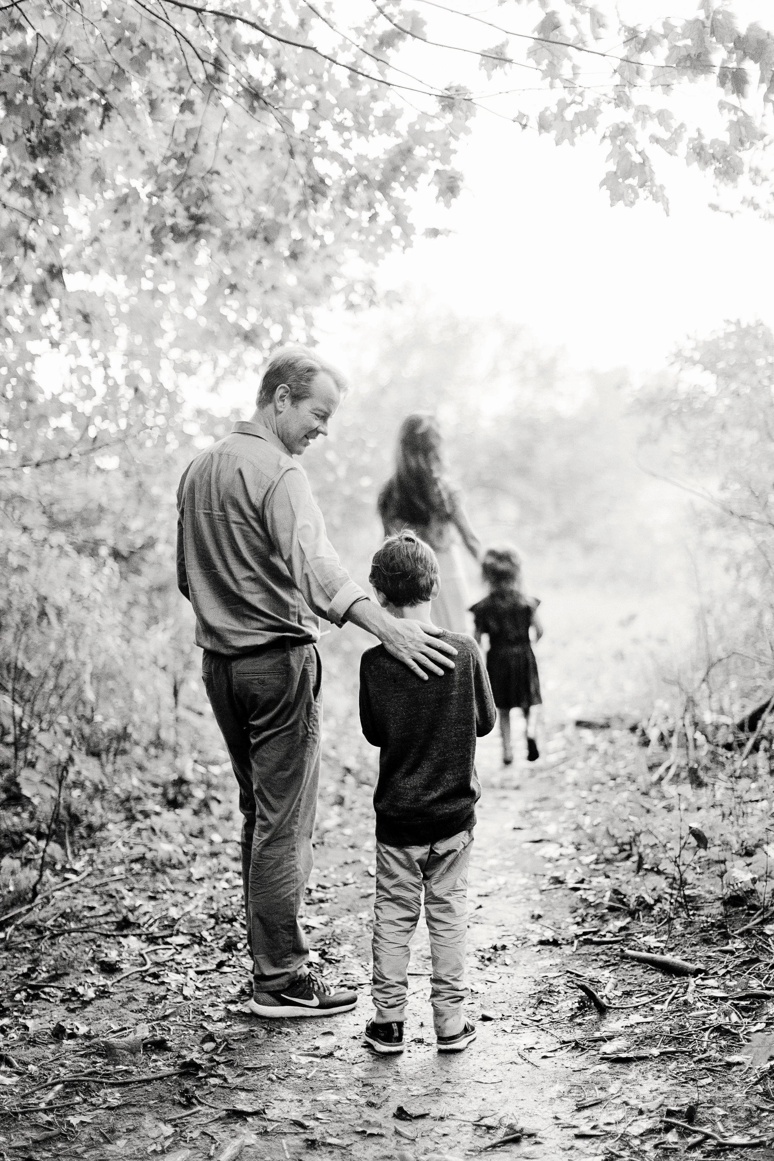 A man and a boy walking on a wooded trail, with a woman and a girl in the background.