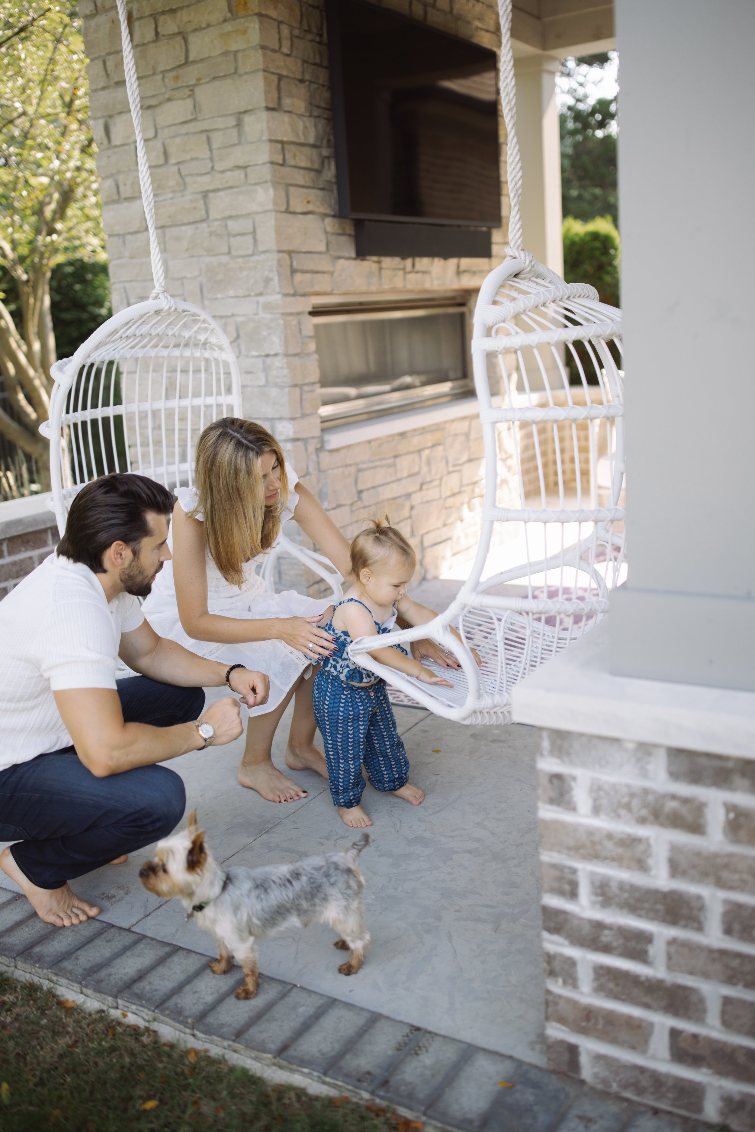 A family with a small child and a dog enjoying time on a patio with hanging chairs.