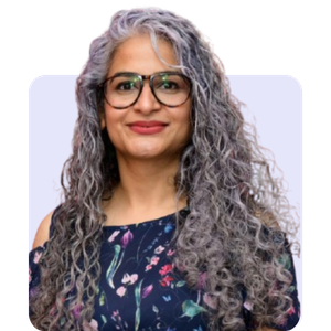 A woman with long curly gray hair, glasses, and a dark floral sleeveless top, smiling at the camera.