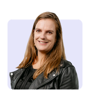 A woman with long brown hair smiling while wearing a black leather jacket against a light background.