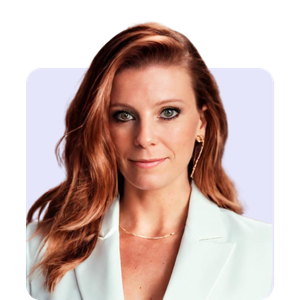 A woman with long, wavy red hair wearing a white blazer and gold earrings, smiling softly against a light-colored background.