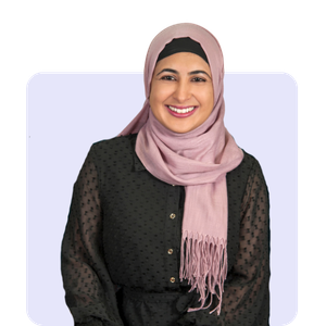 Portrait of a smiling woman wearing a pink hijab and a black textured top, against a light purple background.