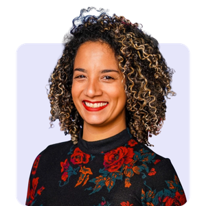 A woman with curly hair smiling, wearing a black top with red floral embroidery, against a light background.