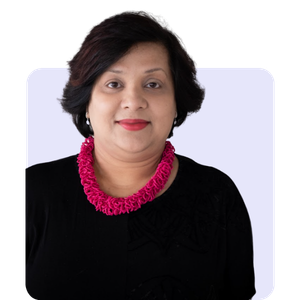 A woman with short black hair wearing a black top and a bright pink beaded necklace, looking at the camera with a neutral expression.