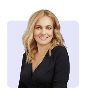 A woman with blonde, wavy hair smiling at the camera against a dark background.