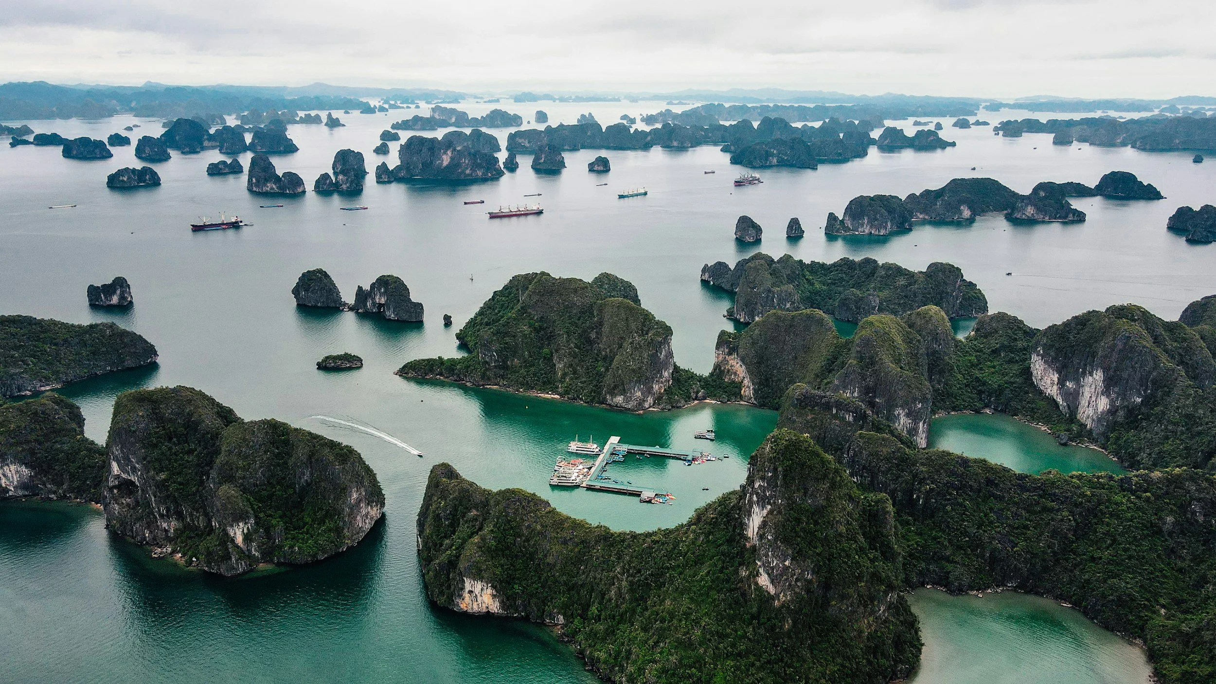Aerial view of limestone karsts and islands in a calm bay, with boats and a small dock in the foreground.
