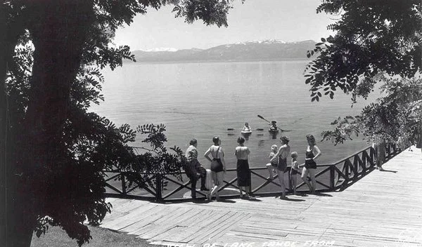 black and white image of swimmers standing on boardwalk by lake
