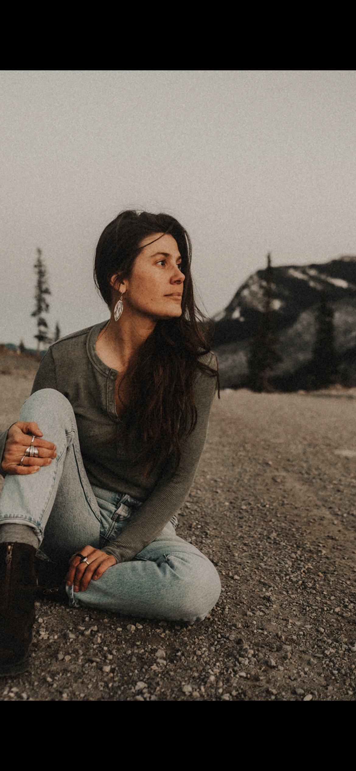 Woman sitting on a rocky outdoor landscape with mountain in the background during dusk or dawn.