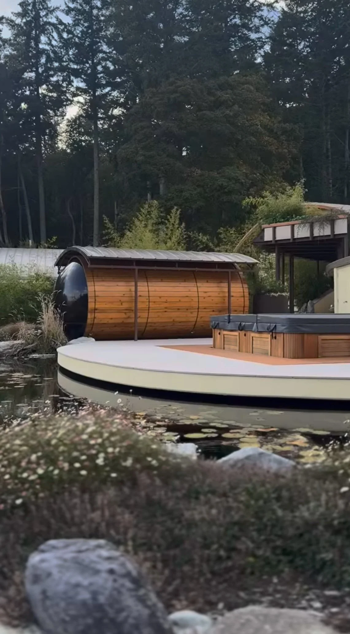 Luxury floating deck with hot tub, surrounded by natural greenery and trees, near a calm pond.