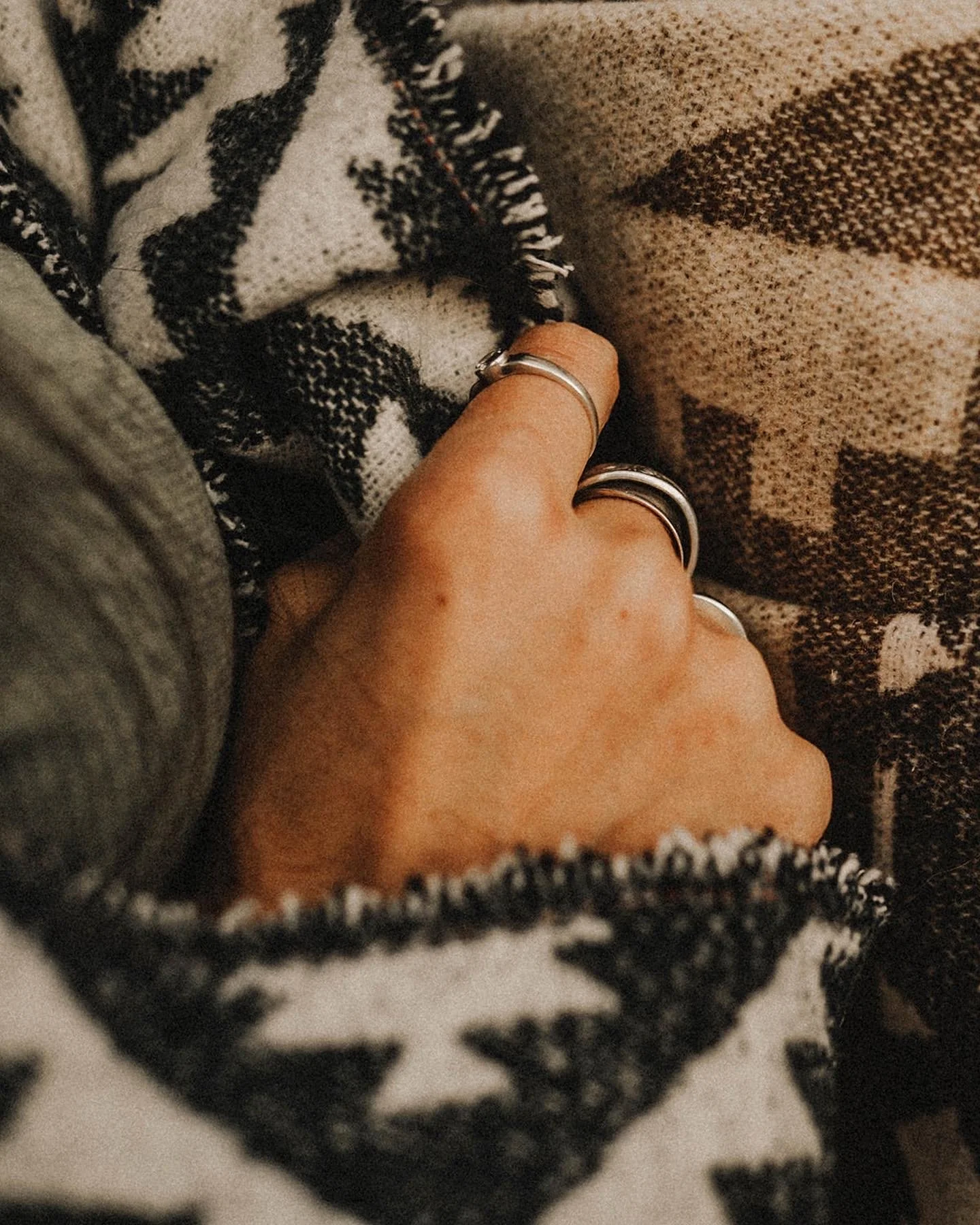A close-up of a person's hand with rings, wrapped in a black and white patterned fabric, and a brown and beige woven textile nearby.