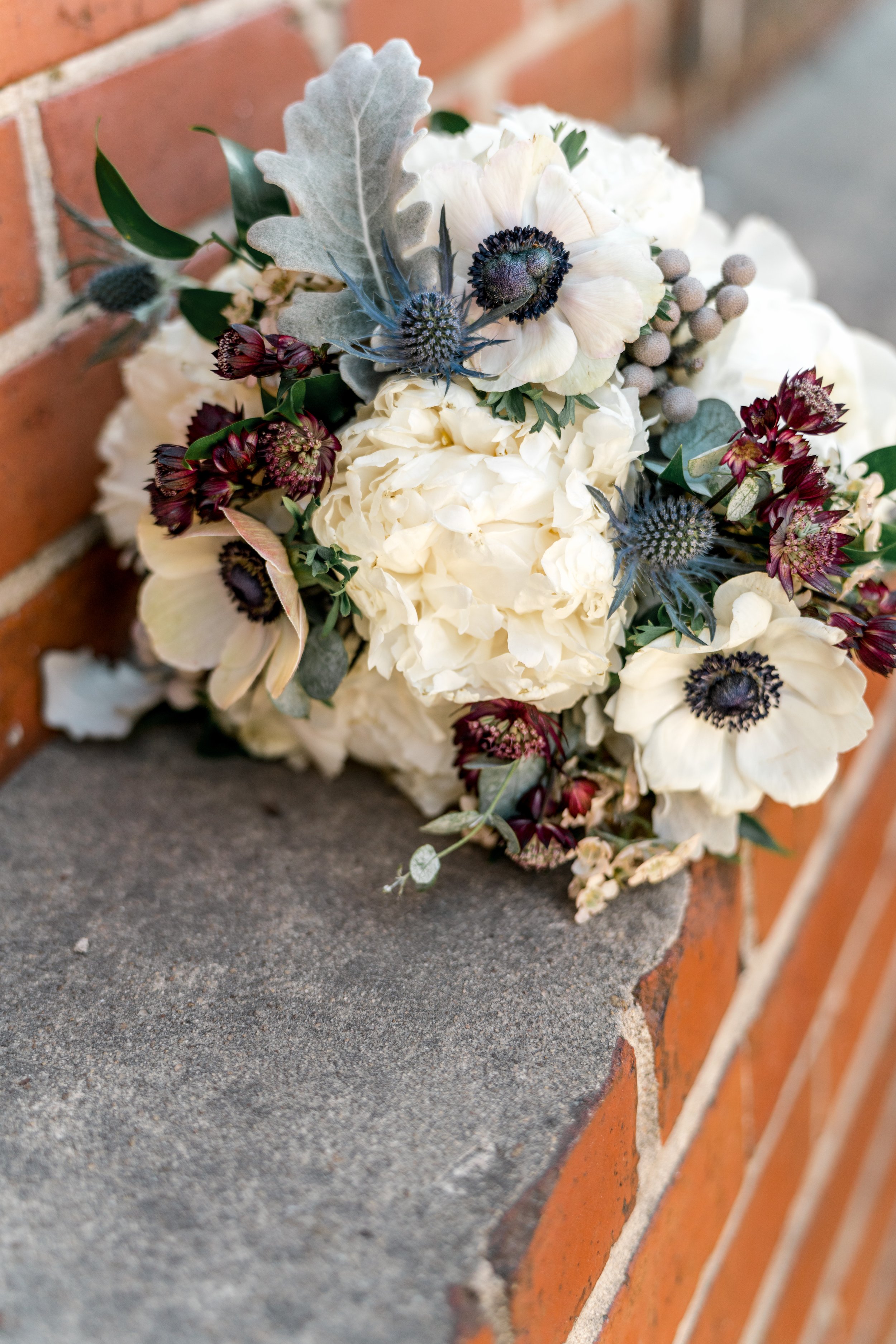 Rustic bouquet with white and burgundy flowers on a brick ledge.