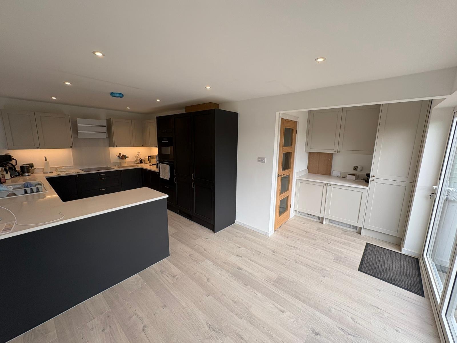 Modern kitchen with light wood flooring, white and black cabinets, and a sliding glass door.