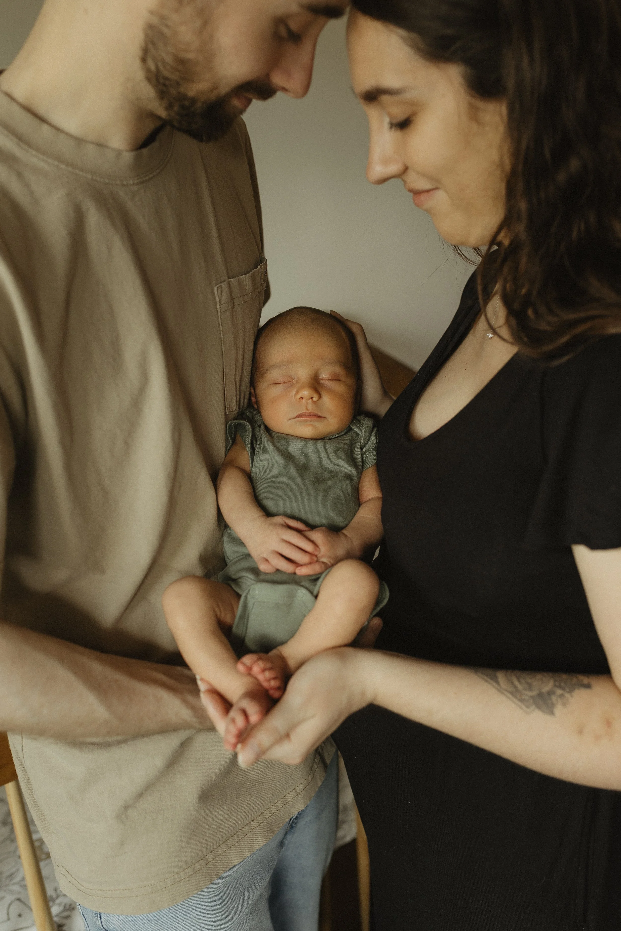 A couple holding a sleeping baby between them, with their foreheads touching, creating an intimate and tender moment.