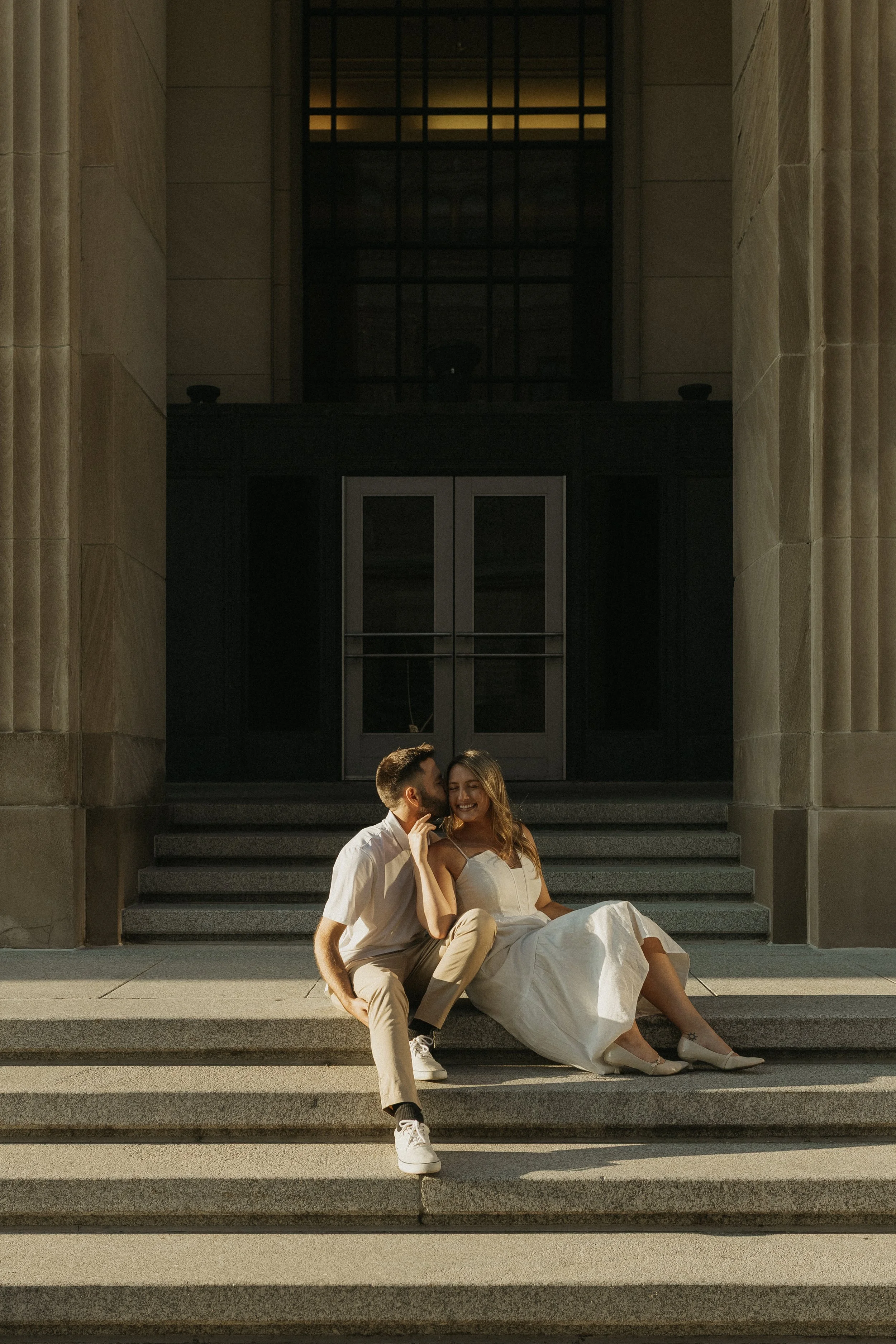 A young couple sitting on steps outside a building, smiling and enjoying each other's company.