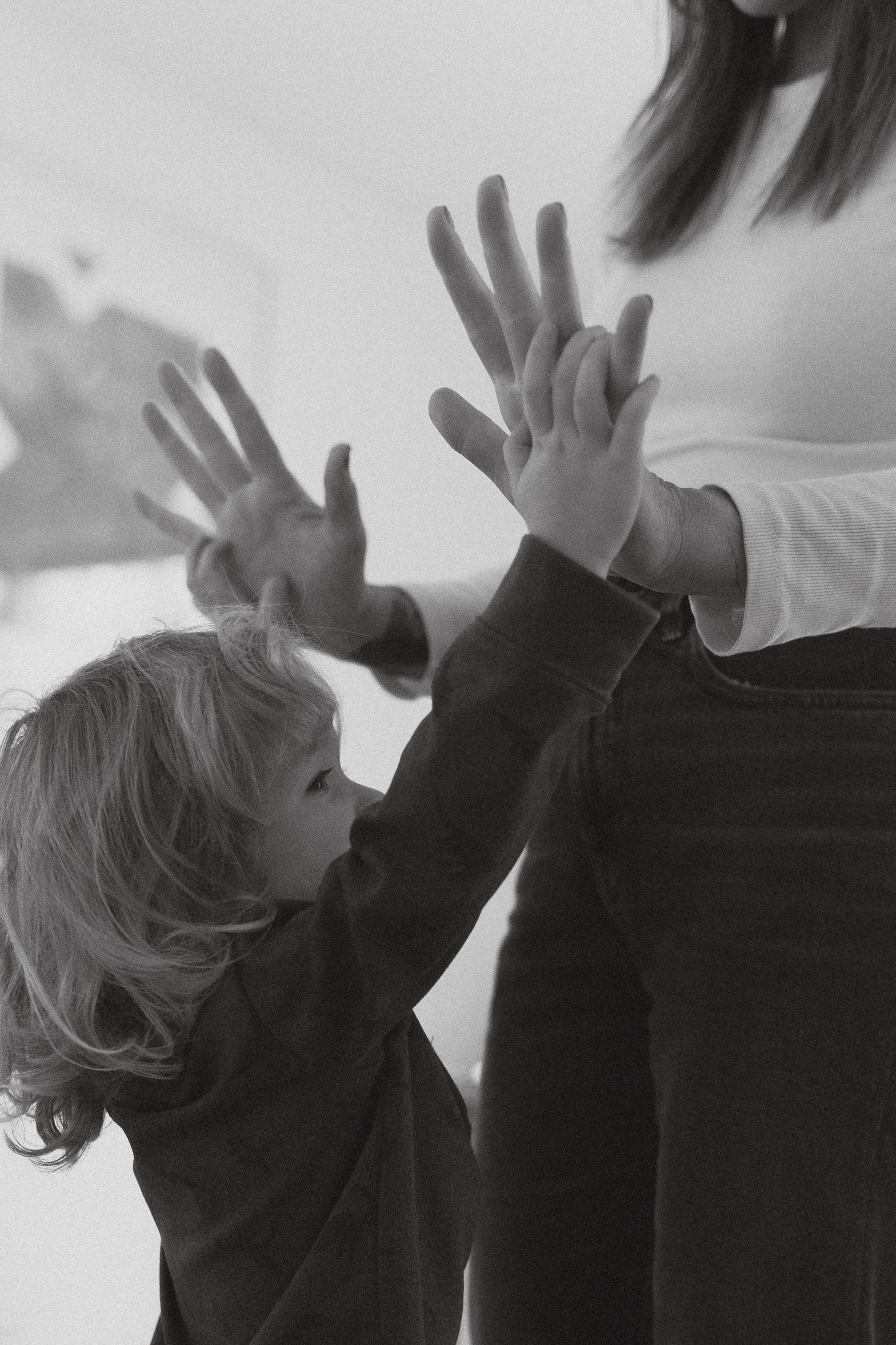 A young child and an adult engaging in a high-five, with the adult's face not visible. The scene appears to be indoors, captured in black and white.