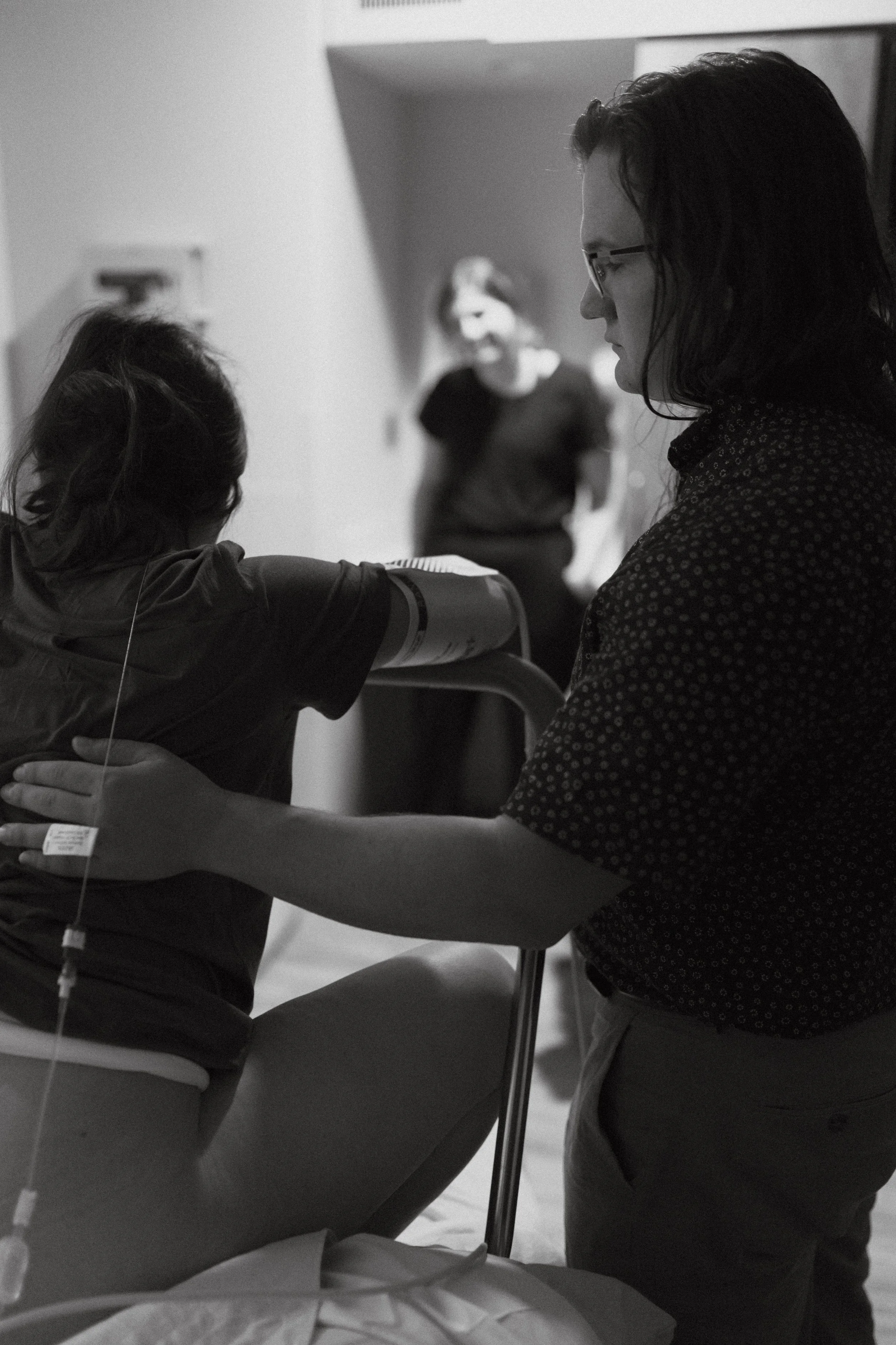A woman laboring in a hospital as a man comforts her with a hand on her back. Image is in greyscale.