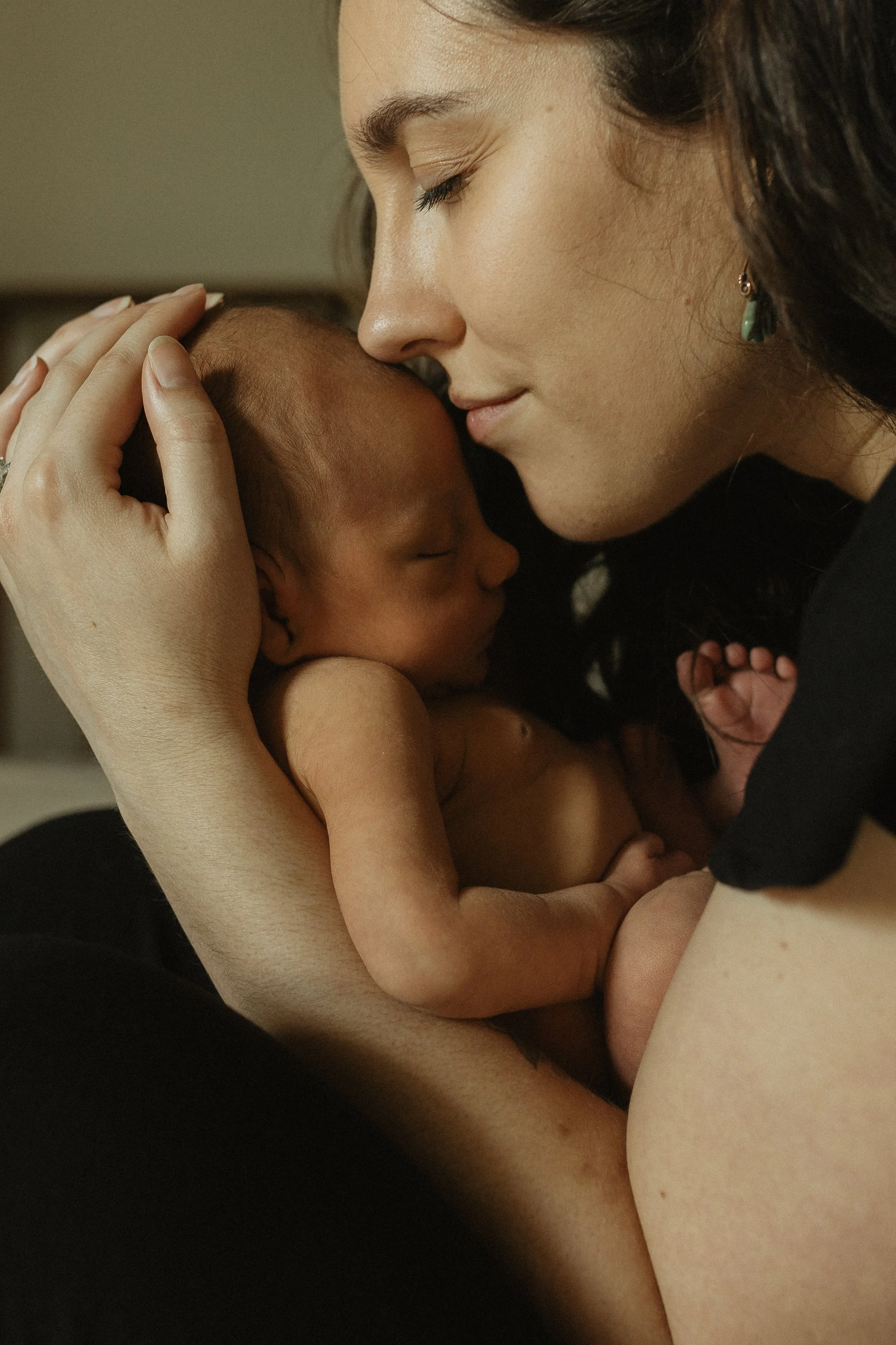 A woman holding a sleeping newborn baby close to her face in an intimate, tender moment.