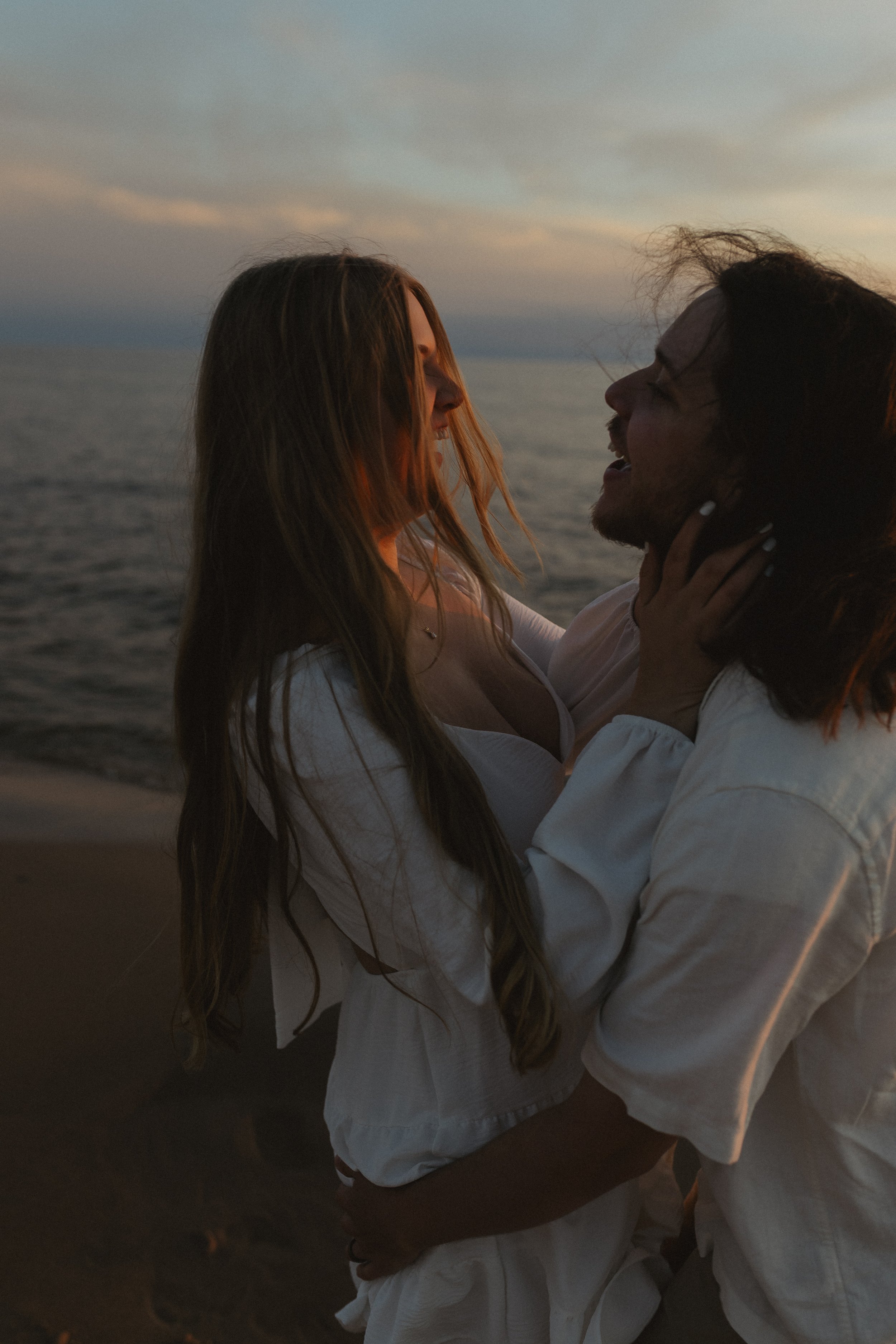 A couple on the beach at sunset, embracing and looking into each other's eyes.