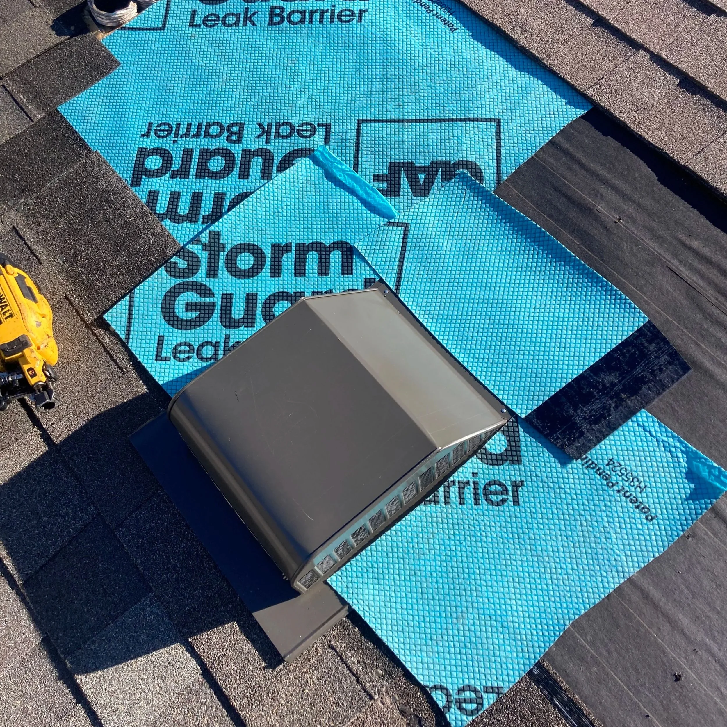 Blue waterproof roof underlayment labeled 'Yakuta Guard Leak Barrier' being installed on a roof. The underlayment is partially overlapped and secured with roofing tools and shingles visible at the edges.