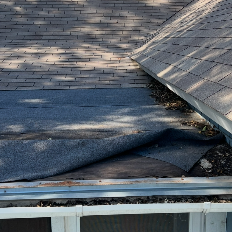 Close-up of a roof with shingles, with a section of damaged roofing material pulled back to reveal underneath layers and debris.