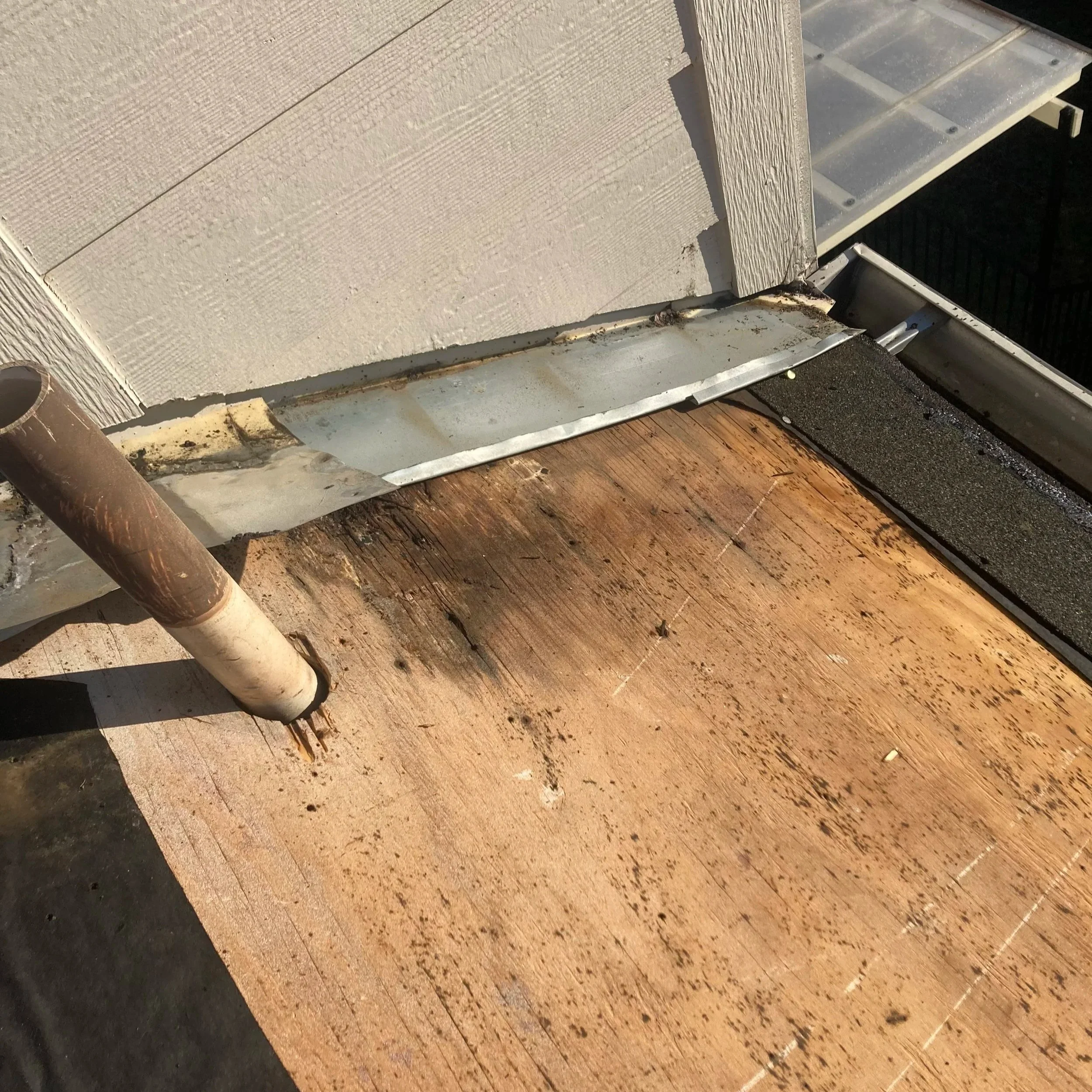 Close-up of a damaged section of a house siding with some dirt and debris around it, showing the edge of the siding and part of a gutter.