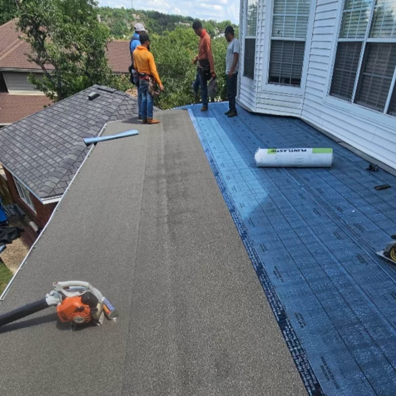 Workers installation a new roof on a house, with blue underlayment visible and roofing tools on the roof.