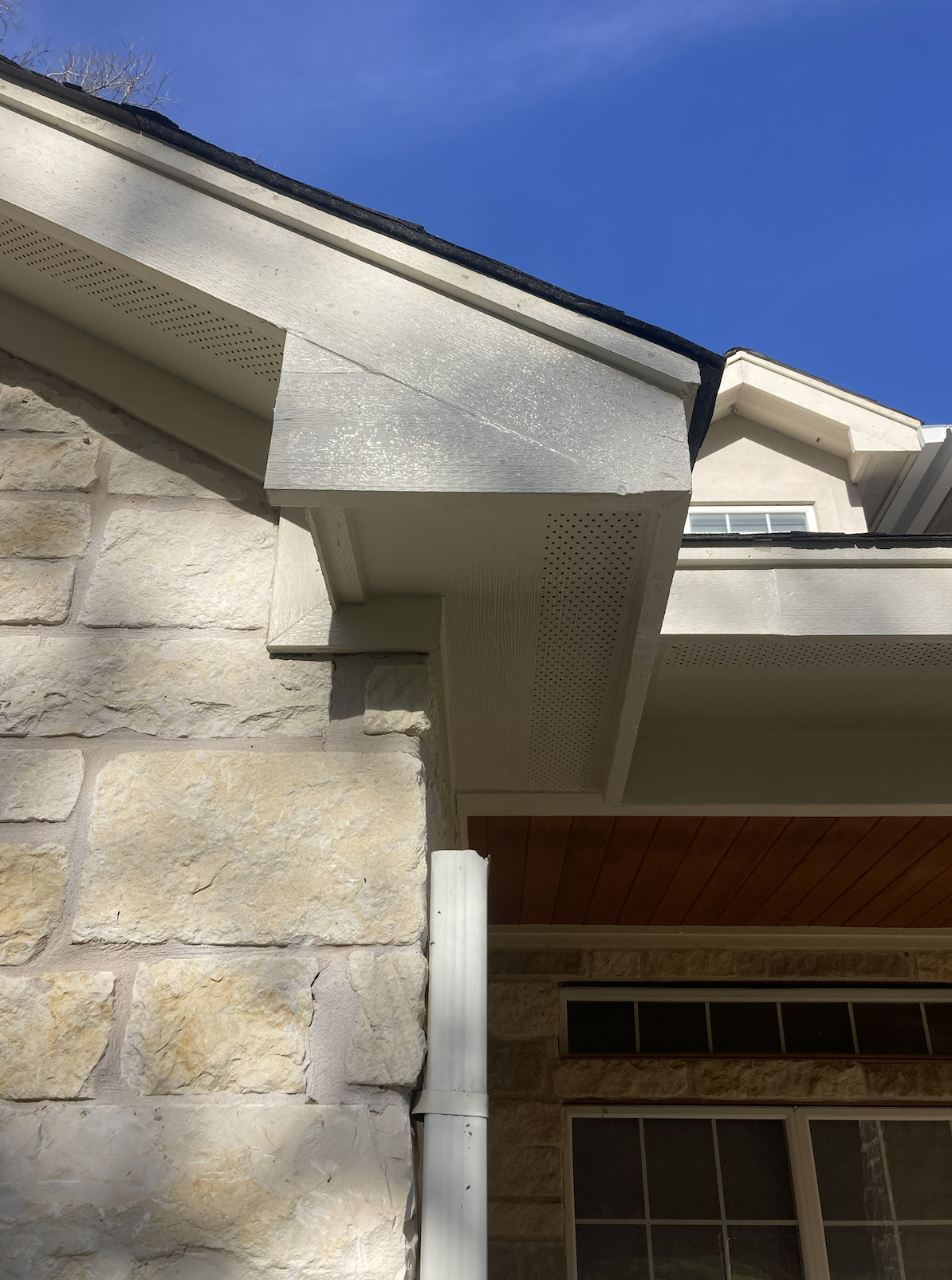 Close-up of the corner of a house showing a stone wall, white soffit, gutter, and part of a window.