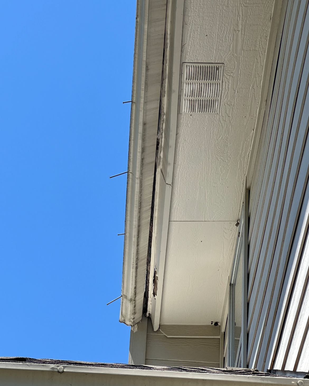 Close-up of a section of a building's exterior wall with a vent and siding, against a clear blue sky.